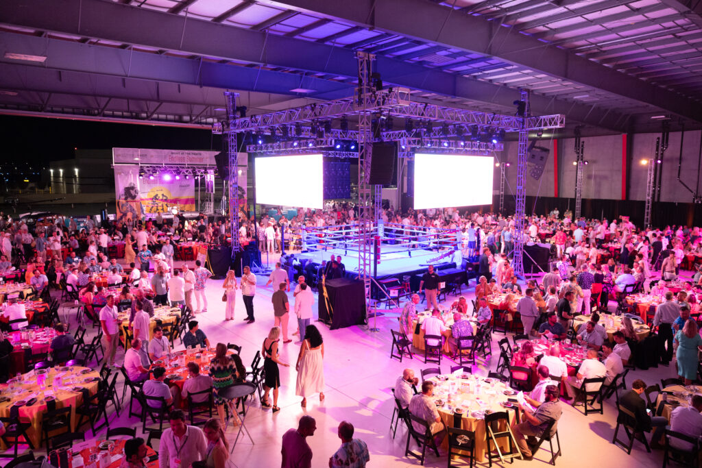 Executive Fight Night: The Ultimate Corporate Experience at Scottsdale Hangar Events Experience the Thrill of Executive Fight NightStep into an unforgettable night of high-level corporate networking, team-building, and top-tier entertainment with Executive Fight Night, an exclusive invite-only event hosted at Scottsdale Hangar Events. This one-of-a-kind experience combines the electrifying energy of live boxing with luxurious design, exceptional service, and unparalleled networking opportunities—all within a uniquely transformed jet hangar. 1. Venue Design & Setup: Transforming the Jet Hangar into a Premier Event Space The Hangar Transformation: Central Boxing Ring: The heart of the event, featuring a dramatically spotlighted boxing ring with custom rigging, high-end lighting, and illuminated runways for unforgettable fighter entrances. VIP Seating: Tiered seating ensures premium visibility, with private VIP sections featuring lounge-style seating, branded tables, and bottle service. Branded Décor: Custom company branding is seamlessly integrated into elegant banners, LED screens, and personalized details such as branded ring corners and digital displays. Lighting Design: A stunning ambiance created with atmospheric lighting, including dramatic spotlights on the ring and warm uplighting throughout the hangar. Luxury Lounges & Networking Spaces: Intimate seating areas with leather furnishings, plush accents, and cocktail tables encourage networking. Aviation-themed décor elements, such as repurposed aircraft parts, add a unique touch of sophistication. 2. Exclusive Experiences & Entertainment Grand Entrances:Fighters, whether corporate participants or professionals, make grand entrances down illuminated aisles with fog effects, dynamic lighting, and custom entrance music. Live Entertainment: Pre-event cocktails feature a live jazz trio or acoustic band. A professional emcee keeps the energy high throughout the bouts. The afterparty includes a live band or DJ to keep the celebration going. Interactive Touchpoints: High-end photo zones with aviation and boxing themes for branded keepsake photos. Virtual Reality (VR) boxing stations for guest engagement. Charity Component:Incorporate a meaningful corporate social responsibility element with donation-driven matches supporting a company-sponsored cause. 3. Gourmet Food & Beverage Offerings Gourmet Catering Stations:Indulge in chef-curated small plates such as steak bites, caviar-topped appetizers, truffle fries, and sushi. Cocktail Experience: Premium open bars with expert mixologists crafting aviation-themed cocktails like "The Jet Fuel Martini." VIP champagne towers and whiskey-tasting stations. Personalized menus, branded cocktail napkins, and customized drinks to elevate the experience. 4. Corporate Branding Integration Customized Ring & Décor:Company branding is integrated throughout the event with personalized seating, digital screens, and ring design. Company Highlights:Showcase corporate milestones and messages using LED screens and projections. Event Keepsakes:Delight guests with branded giveaways such as custom boxing gloves, luxury swag bags, and exclusive merchandise. 5. Entertainment Structure: Event Timeline Program Overview: Guest Arrival: Red carpet welcome with pre-event cocktails and gourmet appetizers. Opening Remarks: Company leadership welcomes attendees and sets the stage for an unforgettable evening. Bout Matches: 3-5 professional and corporate "white-collar" bouts featuring employees for team-building. Mid-Event Show: Live performances, acrobats, dancers, or a charity auction. Post-Event Celebration: A high-energy afterparty with a DJ, dancing, and late-night snacks. 6. Logistics & Production Key Considerations: Obtain all necessary permits and hire professional security to ensure guest safety and seamless crowd management. Partner with an AV production company for lighting, sound, and stage management. Provide VIP transportation options, including valet services, private shuttles, and luxury transportation. 7. Key Event Features Exclusivity: A private, invite-only event catering to top-tier executives, clients, and key team members. Team-Building: Corporate boxing bouts foster camaraderie and morale. Luxury Experience: Every element, from décor to catering and entertainment, exudes sophistication and style. Why Executive Fight Night Works Hosting a corporate boxing event in a jet hangar offers a dynamic and luxurious atmosphere that blends sport, entertainment, and exclusivity. Executive Fight Night provides an unparalleled opportunity to foster meaningful business connections, celebrate achievements, and leave a lasting impression. Ready to Elevate Your Corporate Event?Let us help you bring your vision to life with expert planning, customized branding, and unforgettable experiences. Contact us today to start planning your bespoke Executive Fight Night at Scottsdale Hangar Events.